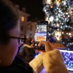 person holding iphone taking photo of lighted christmas tree