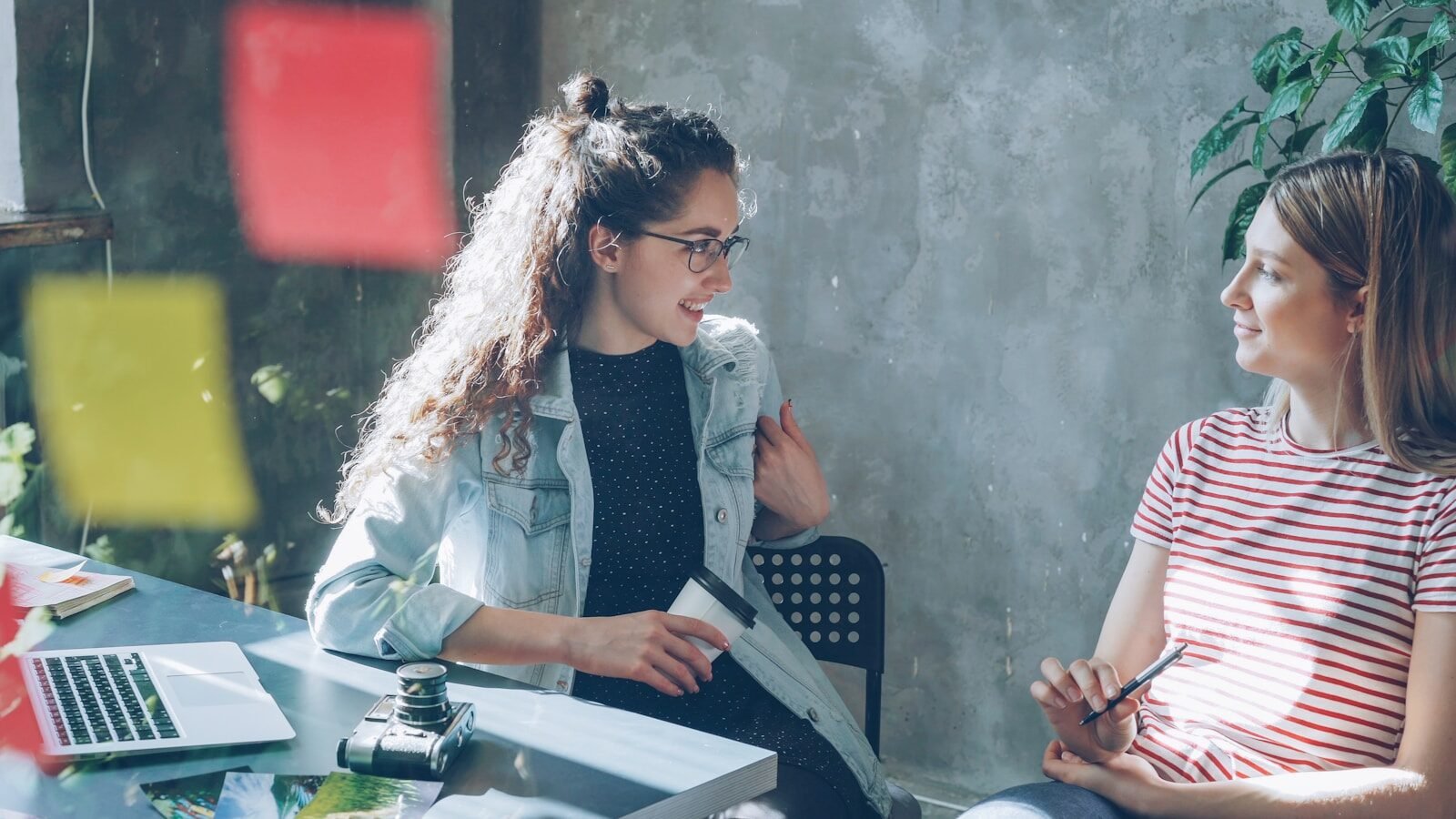 Two women are chatting in a bright office.